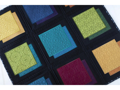 A dark fabric organizer displays nine sets of two stacked, quilted fabric squares in various colors.