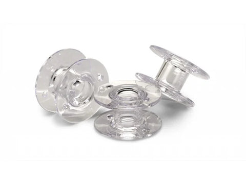 Twelve clear plastic Class 15 bobbins are scattered on a white surface.