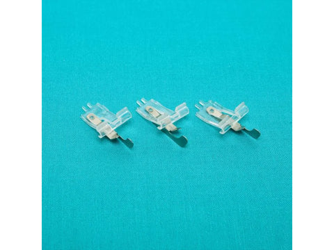 Three clear plastic sewing machine feet with metal components are arranged on a teal fabric.
