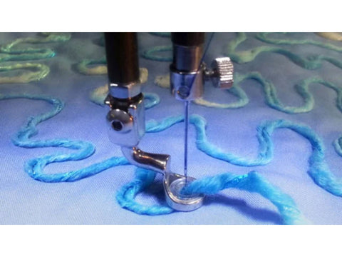 A sewing machine needle and couching foot are stitching blue yarn onto light blue fabric.