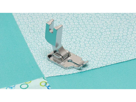 A metal 1/4" quilting foot is positioned on light blue fabric with white circles.