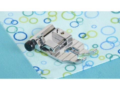 A shiny silver 1/4" quilting foot rests on light blue fabric with colorful circles.