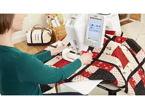 A woman free-motion quilting a red, black, and white quilt on a Baby Lock Alliance machine.