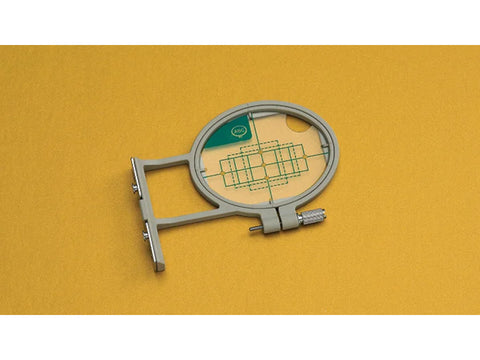 A small, gray embroidery hoop with a clear grid insert on a yellow background.