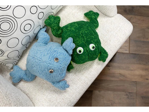 Two plush frog toys, one green and one blue, rest on a textured white couch.