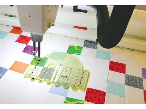 A long arm quilting machine uses a yellow Quilters Select Diameter Arc Ruler on a colorful quilt.