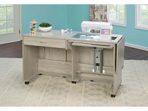 A light wood sewing table with a sewing machine, thread, and a plant on top.
