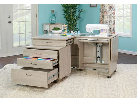 A light wood sewing cabinet with a sewing machine, open drawers, and a companion chest.