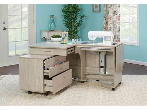 A light wood sewing desk with a sewing machine, open drawers, and a companion chest.