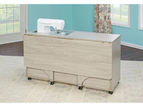 A light wood sewing cabinet with a sewing machine recessed into its top surface.