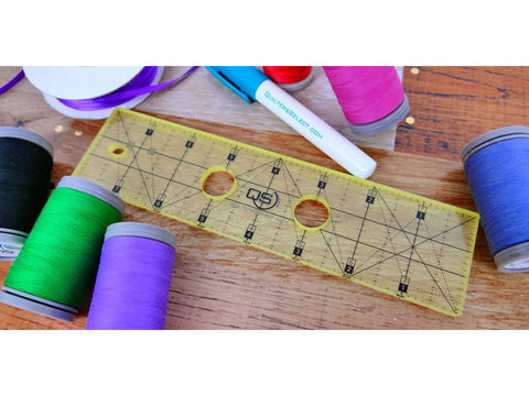 A yellow non-slip quilting ruler with various spools of thread and ribbon.