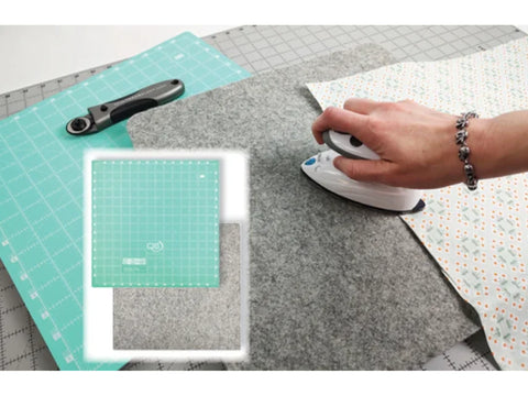A person irons fabric on a wool pressing mat next to a cutting mat and rotary cutter.