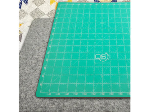 A green cutting mat with white grid lines rests on a gray wool pressing mat.