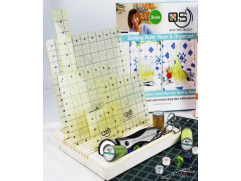 A white wooden quilting ruler rack holds several clear rulers, a rotary cutter, and thread.