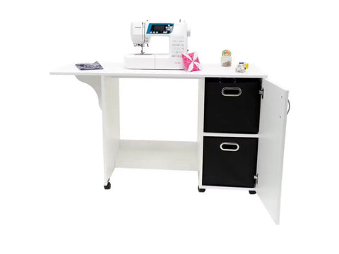 White craft desk with a sewing machine, two black storage bins, and an open cabinet door.