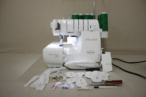 A white Baby Lock Accolade serger with green thread and accessories on a neutral surface.