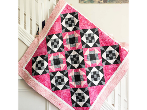 A pink, black, white, and gray Nine Patch Star quilt hangs over a white railing.