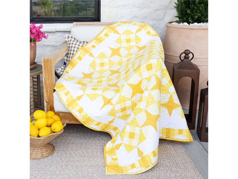A yellow and white star-patterned quilt draped over a wooden outdoor chair.