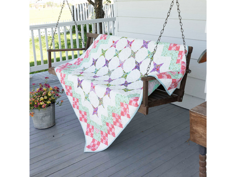 A colorful quilt with a nine-patch star pattern draped over a wooden porch swing.