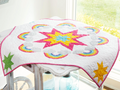 A white quilt with a large pink, yellow, and blue star surrounded by rainbows and clouds.
