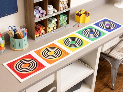 A colorful table runner with five target-like patterns in red, orange, yellow, green, and blue.
