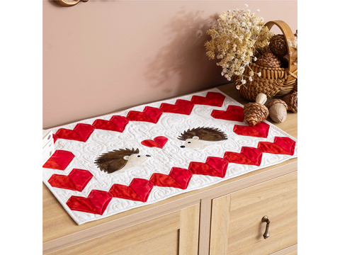 A white quilted table runner with red hearts and two hedgehog appliques.