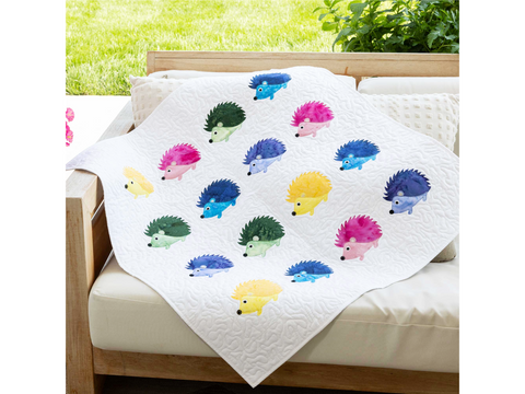A white quilted blanket with colorful hedgehog appliques draped over an outdoor sofa.