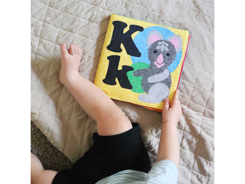 A child holds a yellow felt book with a koala and the letter K.