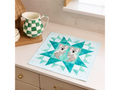 A quilted mat featuring two koalas on a teal star design, with a green checkered pitcher nearby.