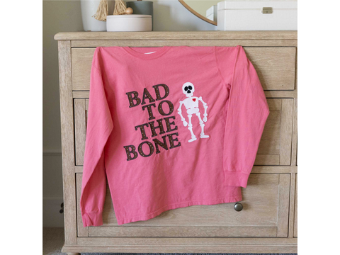 Pink long-sleeve shirt with "BAD TO THE BONE" text and a skeleton graphic.
