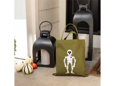 A green tote bag with a white skeleton and red heart design sits on a porch.
