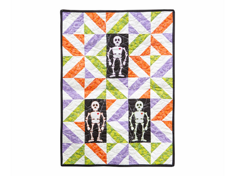 A Halloween-themed quilt features three skeleton figures on a background of colorful geometric patterns.