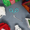 Aqua OESD Alligator Clamps on a grid mat surrounded by lace and fabric projects.