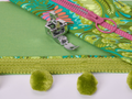 An adjustable zipper and piping foot rests on green fabric next to a pink zipper and green trim.