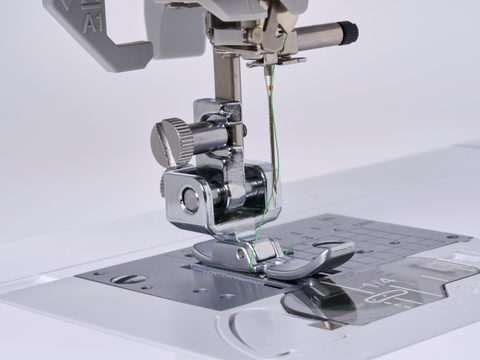 A close-up of a sewing machine's adjustable zipper and piping foot with green thread.