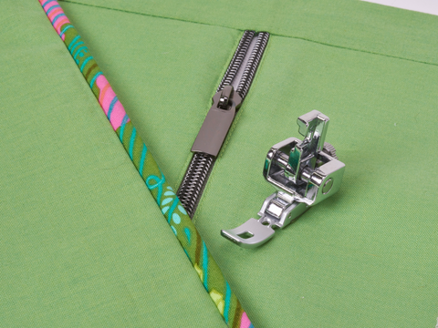 An adjustable zipper and piping foot is shown on green fabric with a zipper and colorful piping.