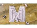A stack of embroidered "M" appliques with floral designs, thread spools, and buttons on a wooden surface.