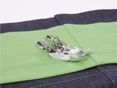 A Baby Lock Jeans Foot is positioned on green fabric, which is sewn to dark blue denim.