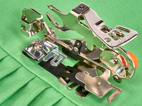 A silver Baby Lock ruffling foot with an orange dial rests on green pleated fabric.