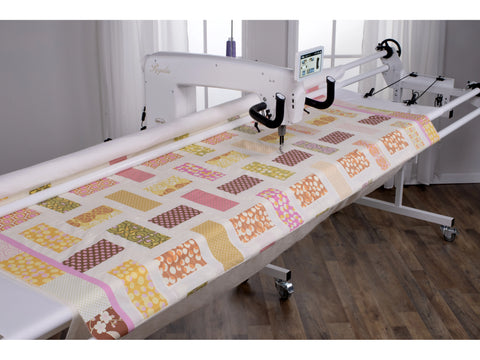 A white Baby Lock Regalia long arm quilting machine on a 12-foot frame with a colorful quilt.