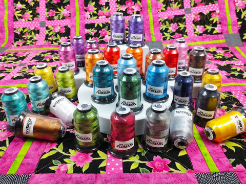 Thirty spools of Floriani embroidery thread in various bold colors are arranged on a floral quilt.