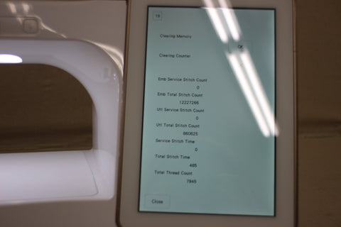 A close-up of a sewing machine's screen displaying stitch counts and service data.