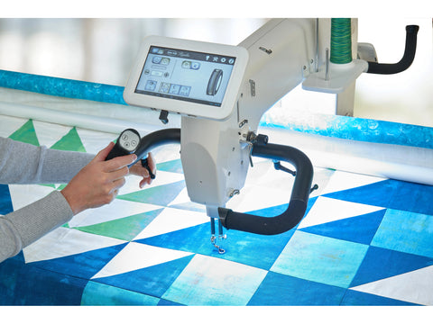 A person operates a white Baby Lock Regalia long arm quilting machine on a blue and white quilt.