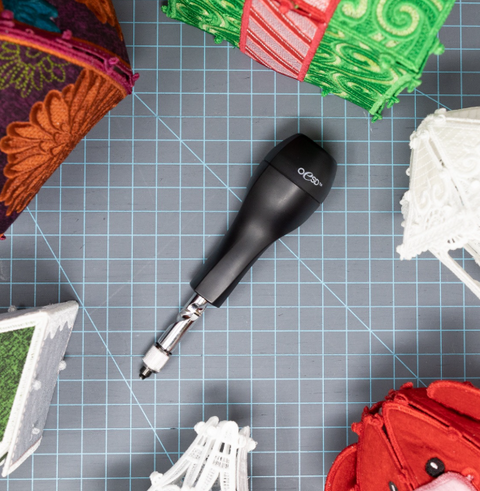 A black OESD Perfect Punch tool rests on a gray cutting mat surrounded by embroidery projects.