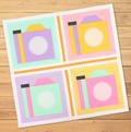 A quilt-as-you-go kit features four pastel camera quilt blocks on a wooden surface.